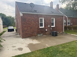 A brick house with a satellite dish, a car parked in the driveway, and a small trash bin. - Family Vacation house (Redford)