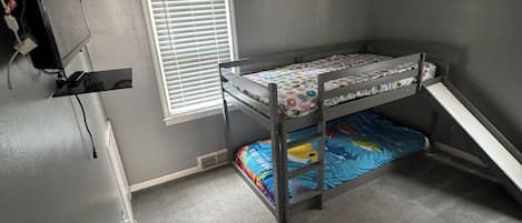 A room with a bunk bed, a window with blinds, a wall clock, and a ceiling light fixture.
