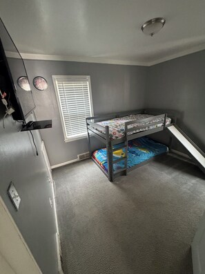 Ein Zimmer mit einem Etagenbett, einem Fenster mit Jalousien, einer Wanduhr und einer Deckenleuchte.
