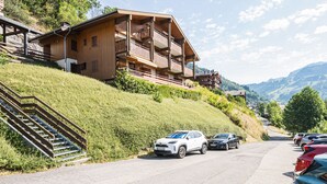 Eine Holzhütte mit Balkonen, einer Treppe und einem Parkplatz mit Autos.