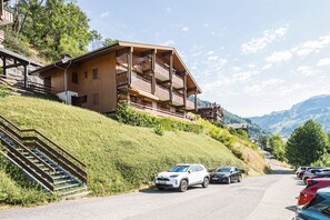 A wooden chalet with balconies, a staircase, and a parking area with cars. - Le Prés Vieux - Appt avec balcon et vue montagne (Le Grand Bornand)