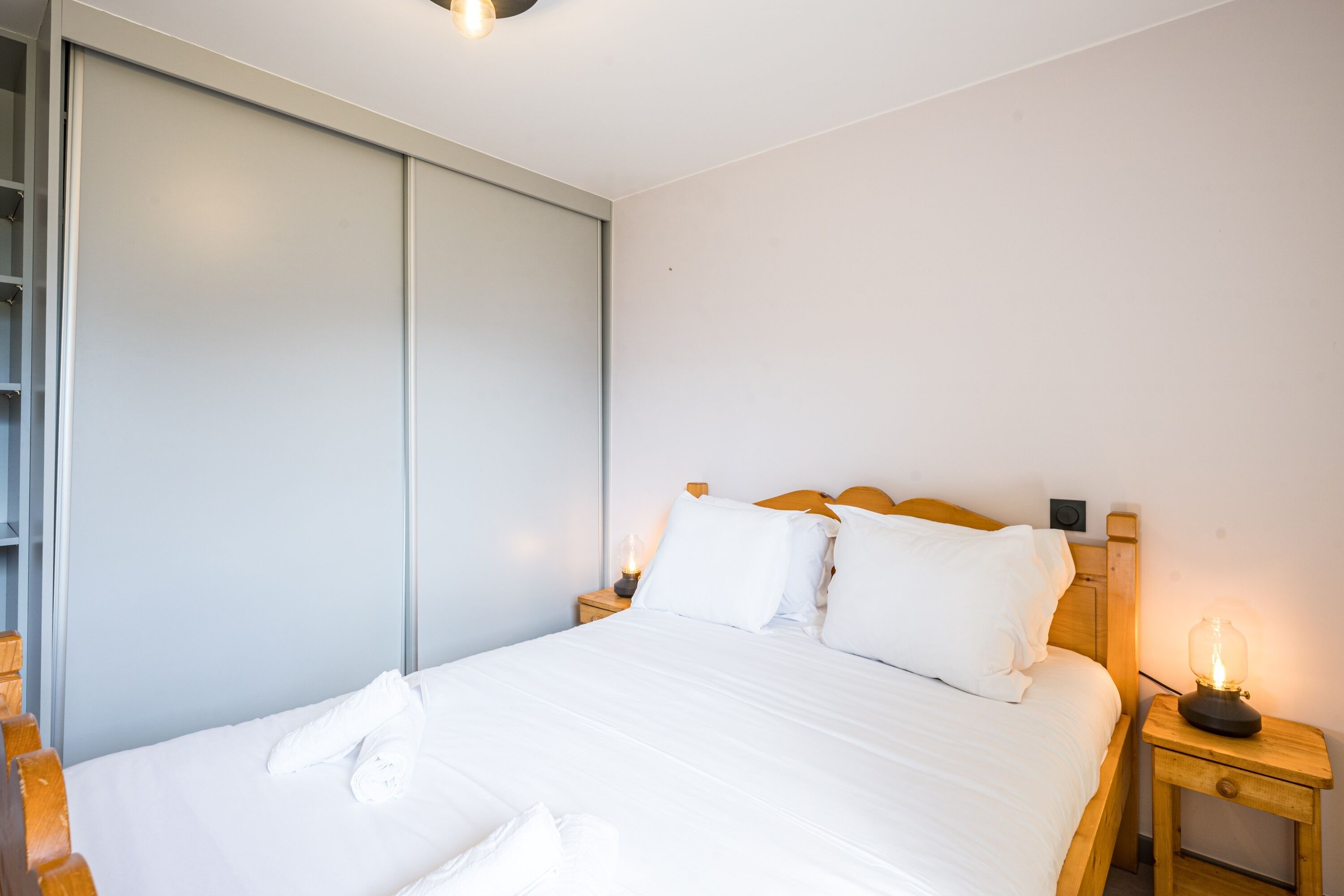 A neatly made bed with white linens, a wooden headboard, and a bedside table with a lamp.