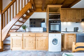 Une cuisine avec des meubles en bois, un lave-linge, un four à micro-ondes et un escalier en bois.