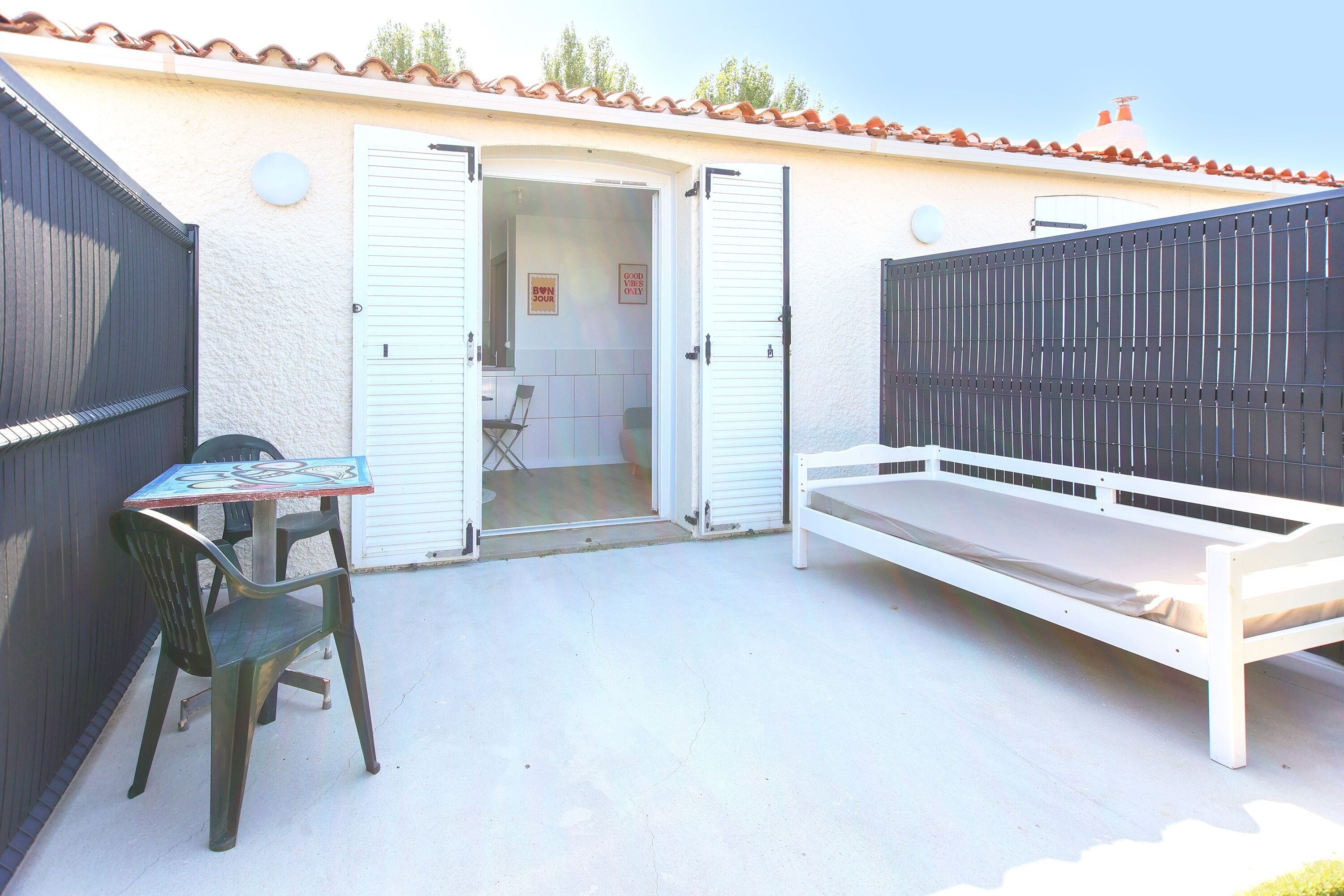 Eine Terrasse mit Tisch und Stühlen, eine weiße Bank und eine teilweise geöffnete Tür zu einem Innenbereich.