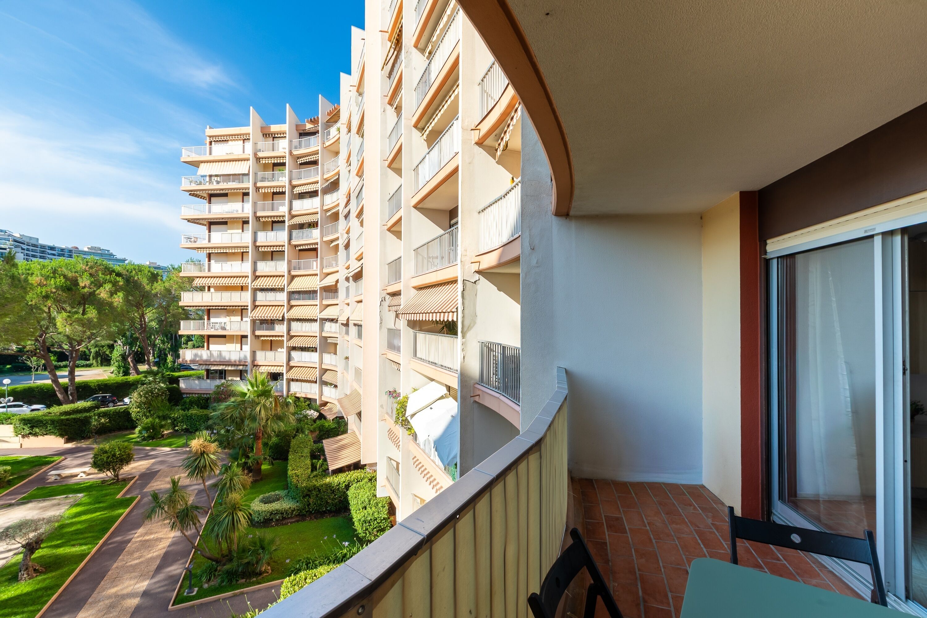 A balcony with a view of a multi-story building, a tiled floor, and a chair.