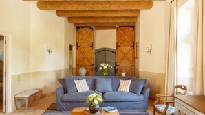 A room with a blue sofa, wooden ceiling beams, a bench, a wooden dresser, and a large wooden door. - Pézenas Mill (Pézenas)