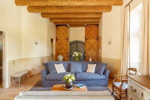 Ein Zimmer mit einem blauen Sofa, Holzbalkendecke, einer Bank, einem Holzschrank und einer großen Holztür.