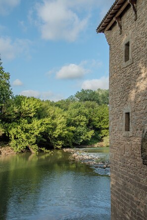 Ein Gebäude aus Stein mit einem Ziegeldach, einem Fluss und dichtem, grünem Grün im Hintergrund.