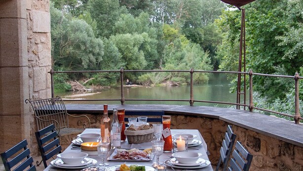 An outdoor dining area with a table set for two, surrounded by stone walls and a view of a body of water. - Pézenas Mill (Pézenas)