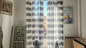 Quarto com vista através de uma cortina listrada, um radiador, um quadro na parede e um letreiro com uma frase motivacional.