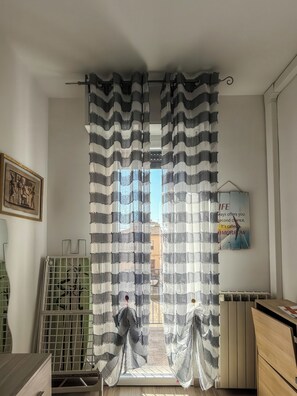 Una habitación con vistas a través de una cortina a rayas, un radiador, un cuadro en la pared y un letrero con una cita motivacional.