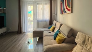 Uma sala de estar com sofá, mesa de centro, televisão e porta de vidro deslizante que dá para uma área externa.