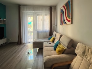 Una sala de estar con sofá, mesa de centro, televisor y puerta corrediza de vidrio que da a un área exterior.