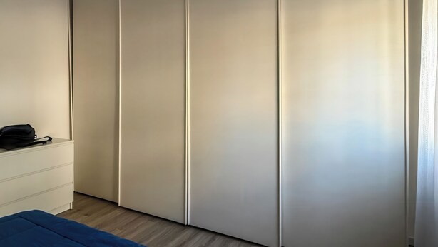Quarto com guarda-roupa, mesa de cabeceira e colcha azul.