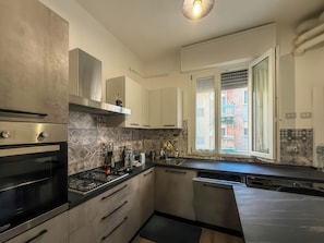 Una cocina moderna con electrodomésticos de acero inoxidable, lavavajillas y ventana con vista a un edificio.