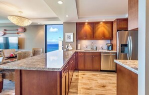 Eine moderne Küche mit Holzschränken, einem Edelstahl-Kühlschrank und einer großen Kochinsel mit Granit-Arbeitsplatte.