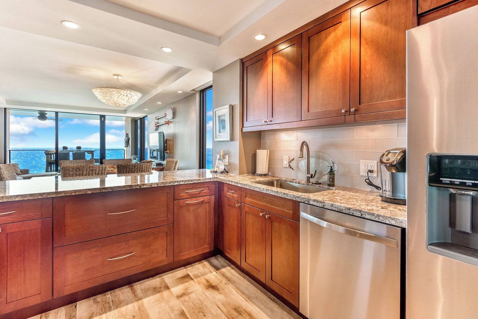 A modern kitchen with wooden cabinets, stainless steel appliances, and a large window overlooking the ocean.