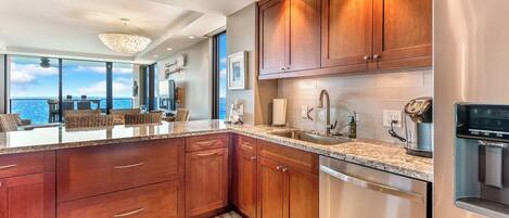 A modern kitchen with wooden cabinets, stainless steel appliances, and a large window overlooking the ocean.