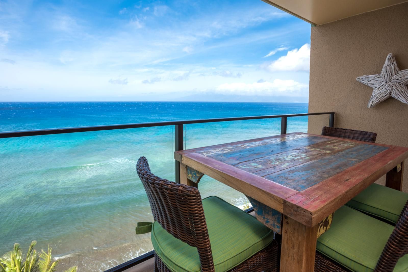 A wooden table with green cushions on a balcony overlooking a clear blue sea.