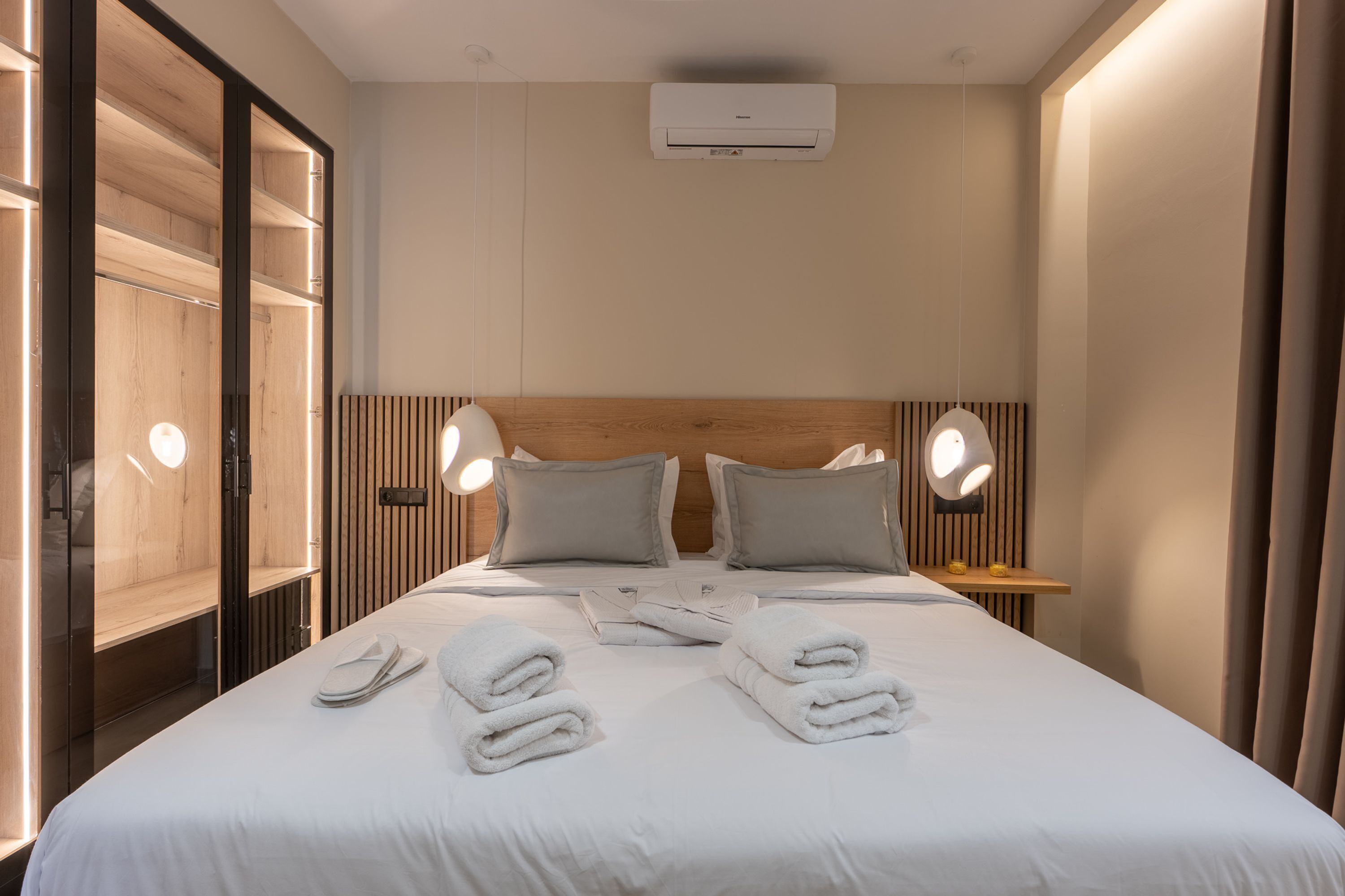 Habitación de hotel con cama, dos lámparas de noche, cabecero de madera, mesita de noche y aire acondicionado instalado en la pared.