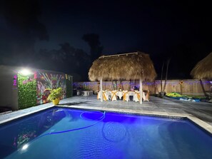 Ein Swimmingpool mit einer strohgedeckten Struktur und Tischen, die für Speisen eingerichtet sind.
