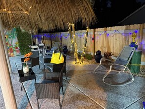An outdoor patio with wicker furniture, a thatched roof, and decorative lights.