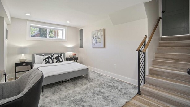 Un dormitorio con cama, mesitas de noche, una silla, ventana, un cuadro y una escalera.