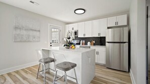 Una cocina moderna con muebles blancos, un refrigerador de acero inoxidable y una isla de mármol con dos taburetes de bar.