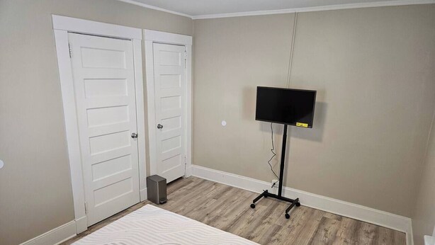 Ein Schlafzimmer mit einem Bett, zwei weißen Türen, einem Fernseher auf einem Schrank und einer kleinen Mülltonne.