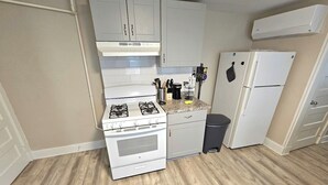 Eine Küche mit weißen Schränken, einem Gasherd, einem Kühlschrank und einer Mülltonne.