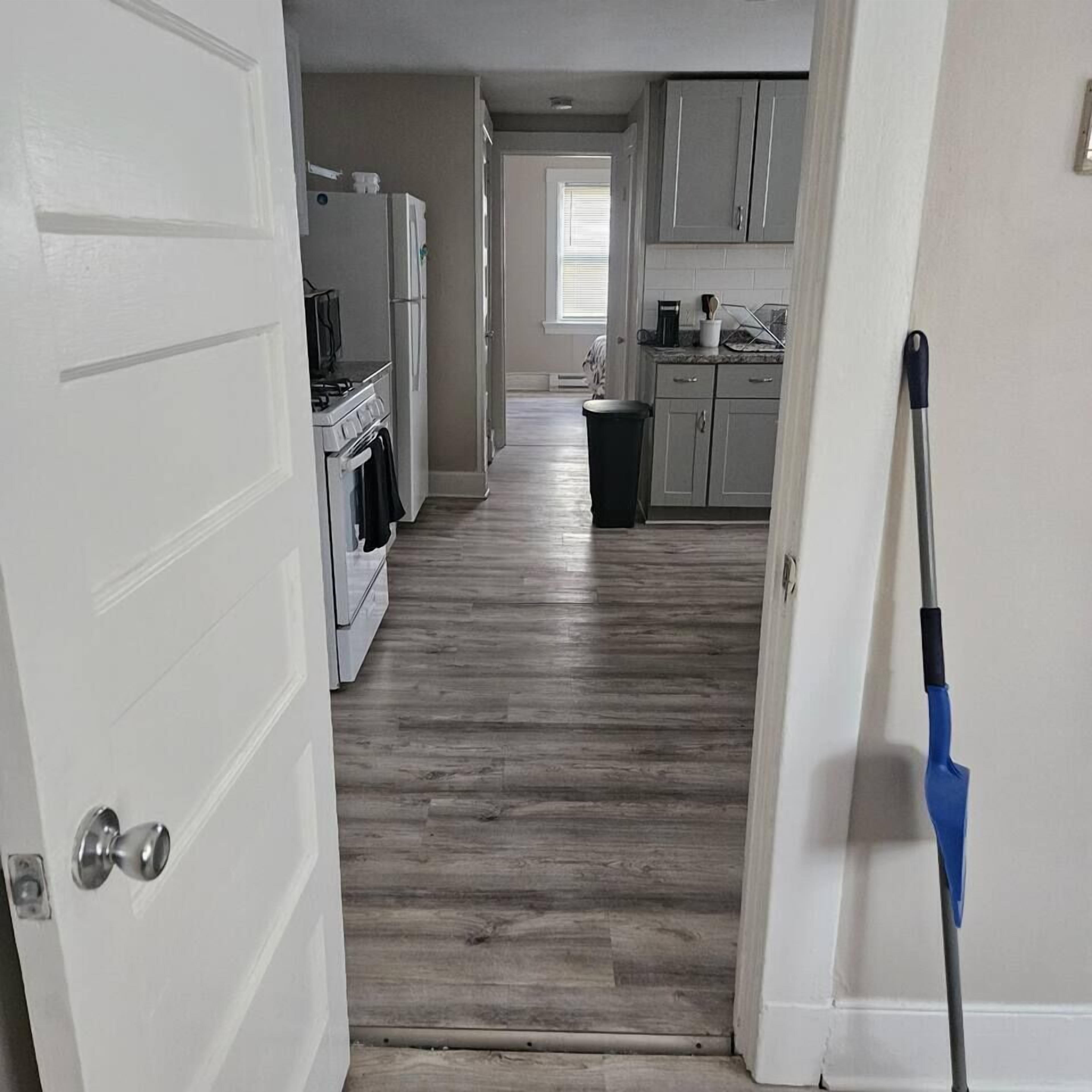A hallway with a kitchen area, including cabinets, a refrigerator, and a stove.