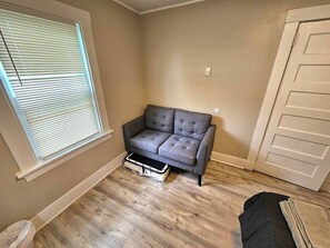 A room with a grey sofa, a window with blinds, a door, and a trash bin. - Montclair 1st flr Apt/w Porch|Easy Access to NYC (Montclair)