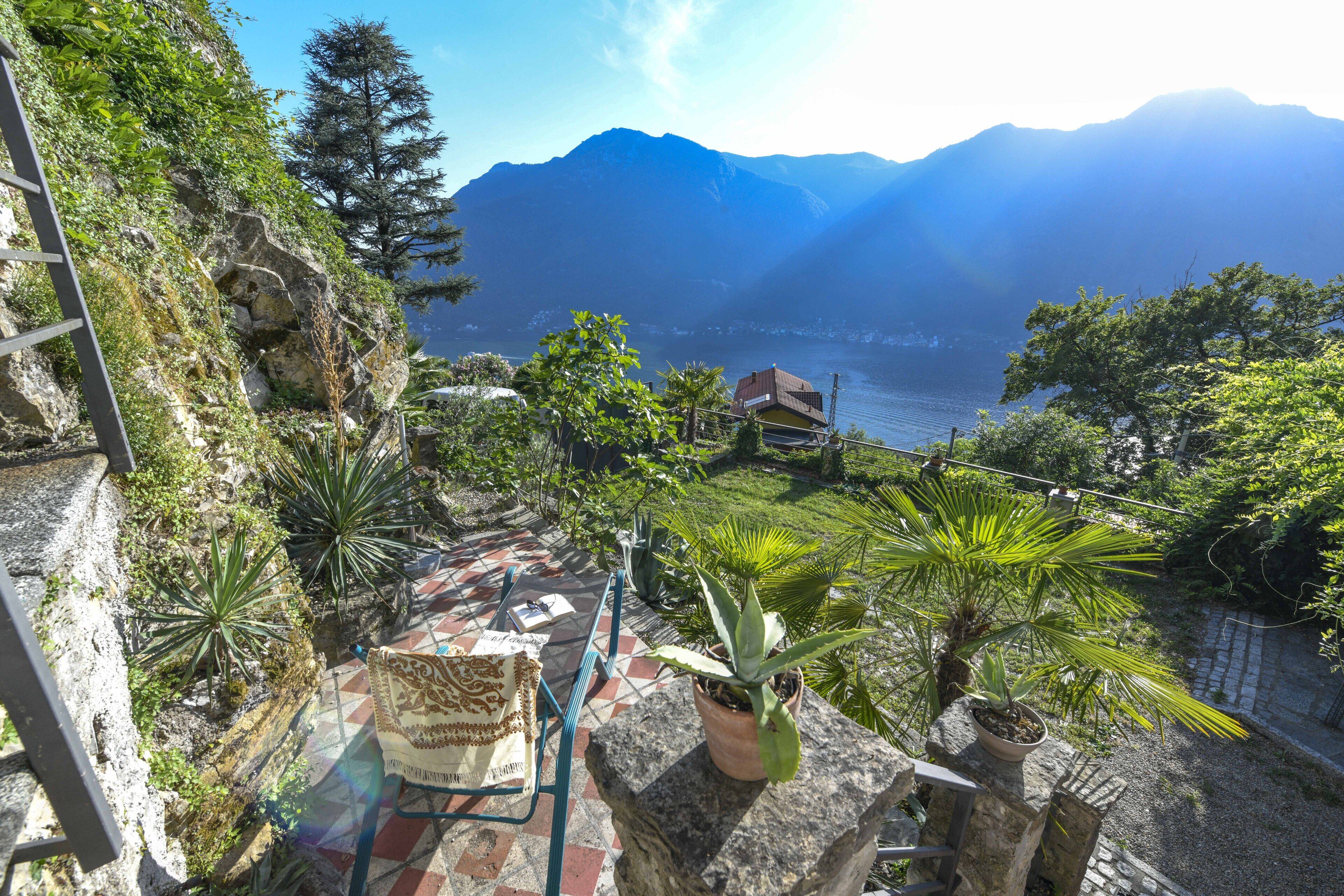 Una terraza con plantas en macetas, una silla y vistas a montañas y un lago.