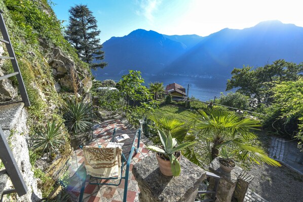 Una terraza con plantas en macetas, una silla y vistas a montañas y un lago.