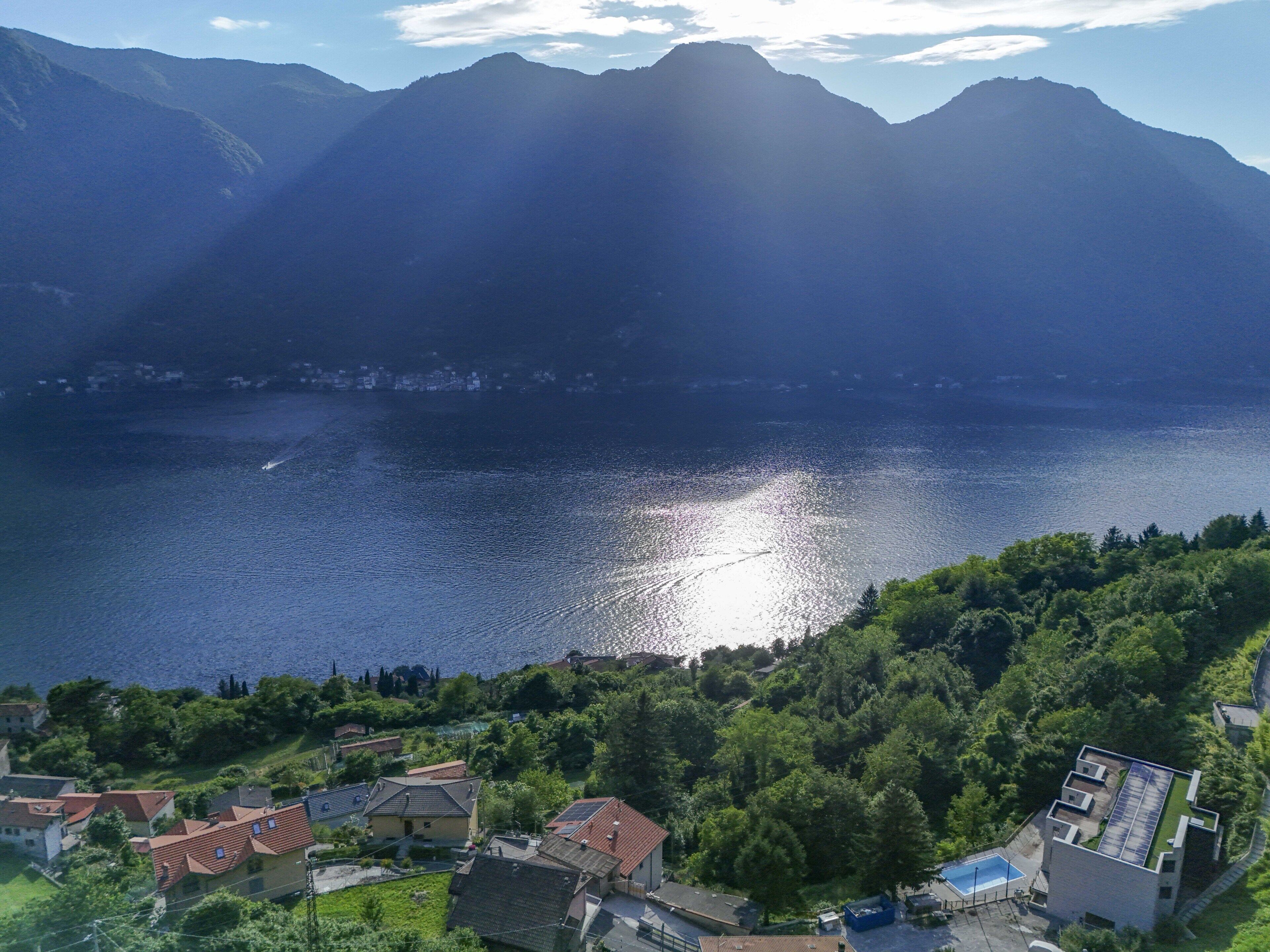 A lake with mountains in the background, surrounded by residential buildings with red roofs.