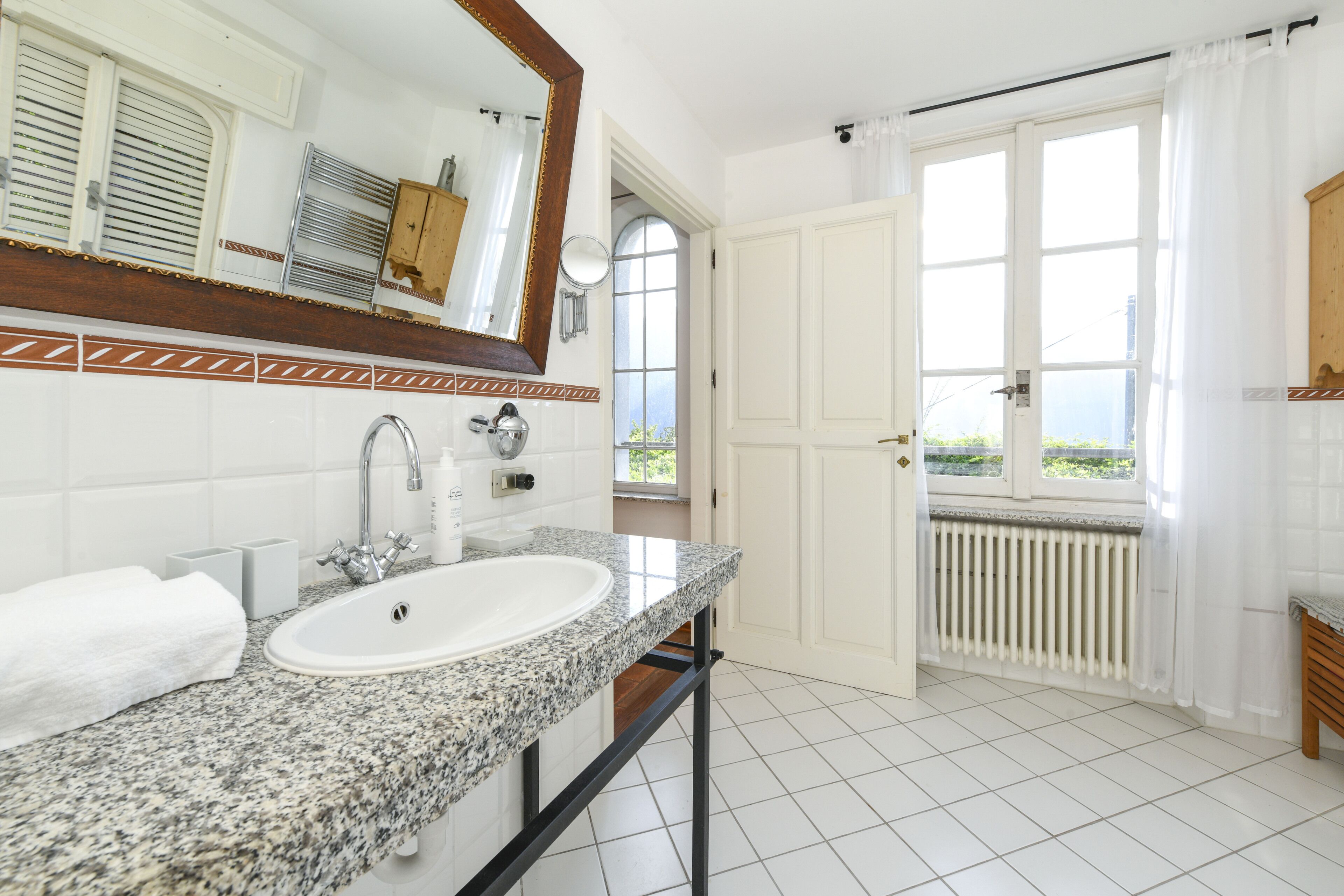 Un baño con lavamanos de encimera de granito, un espejo y vistas al exterior a través de una puerta.