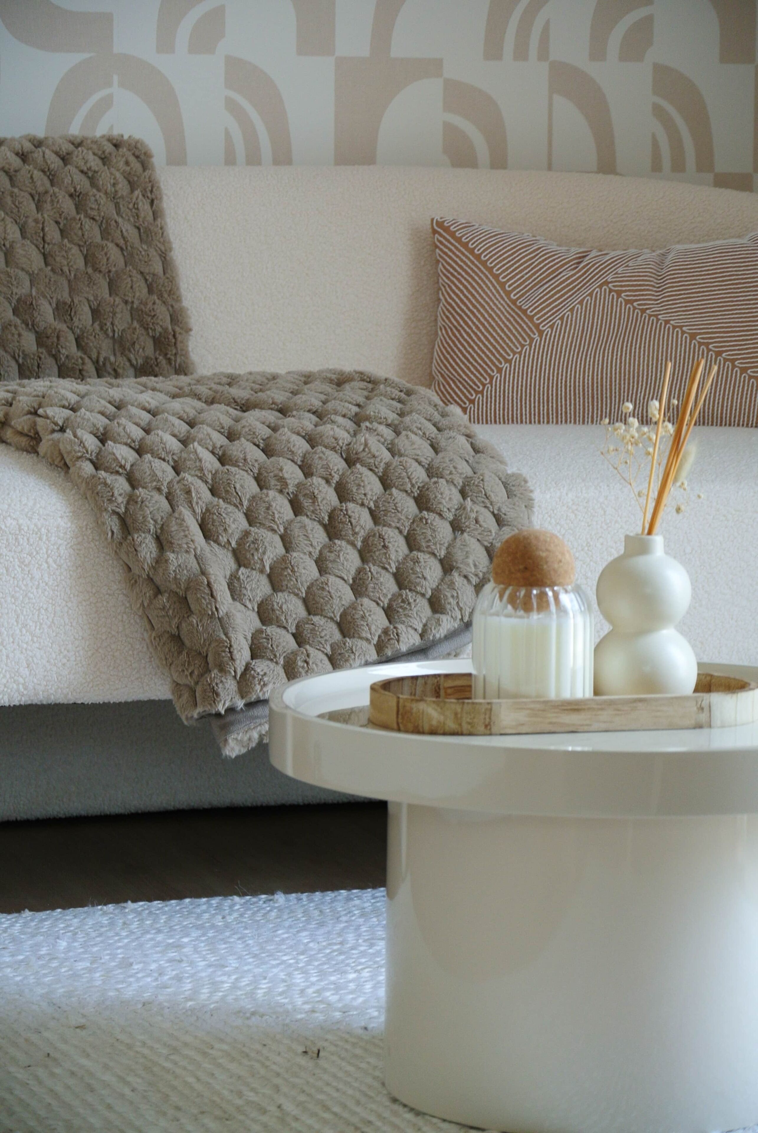 Een gezellige woonkamer met een bank, een gebreide plaid, een gestreept kussen en een klein tafeltje met decoratieve objecten.