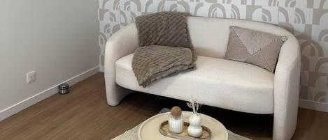 Una sala de estar moderna con papel tapiz estampado, un sofá beige con cojines y una mesa de centro redonda con objetos decorativos.