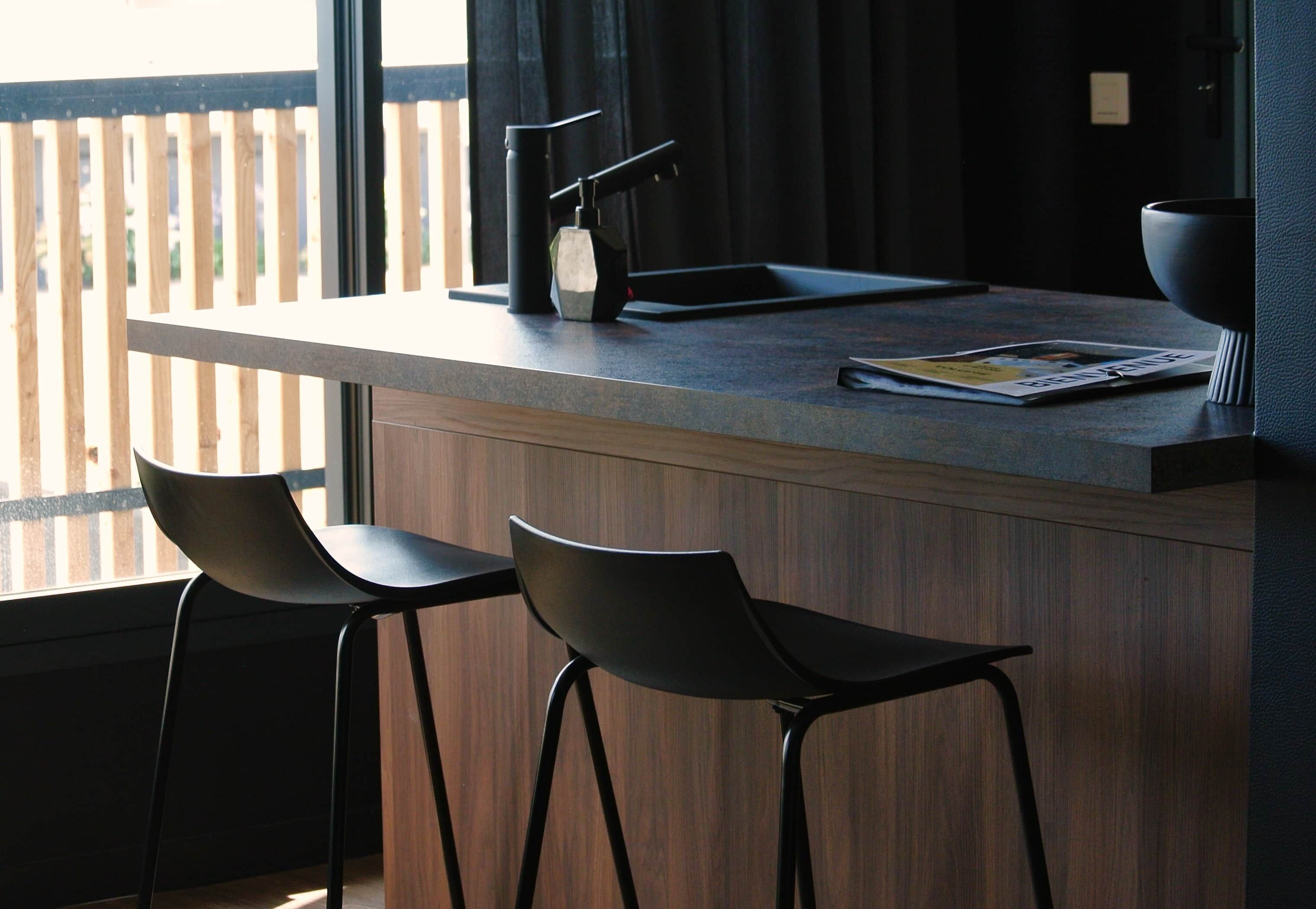 Una cucina moderna con angolo bar, due sgabelli da bar neri e una rivista sul bancone.