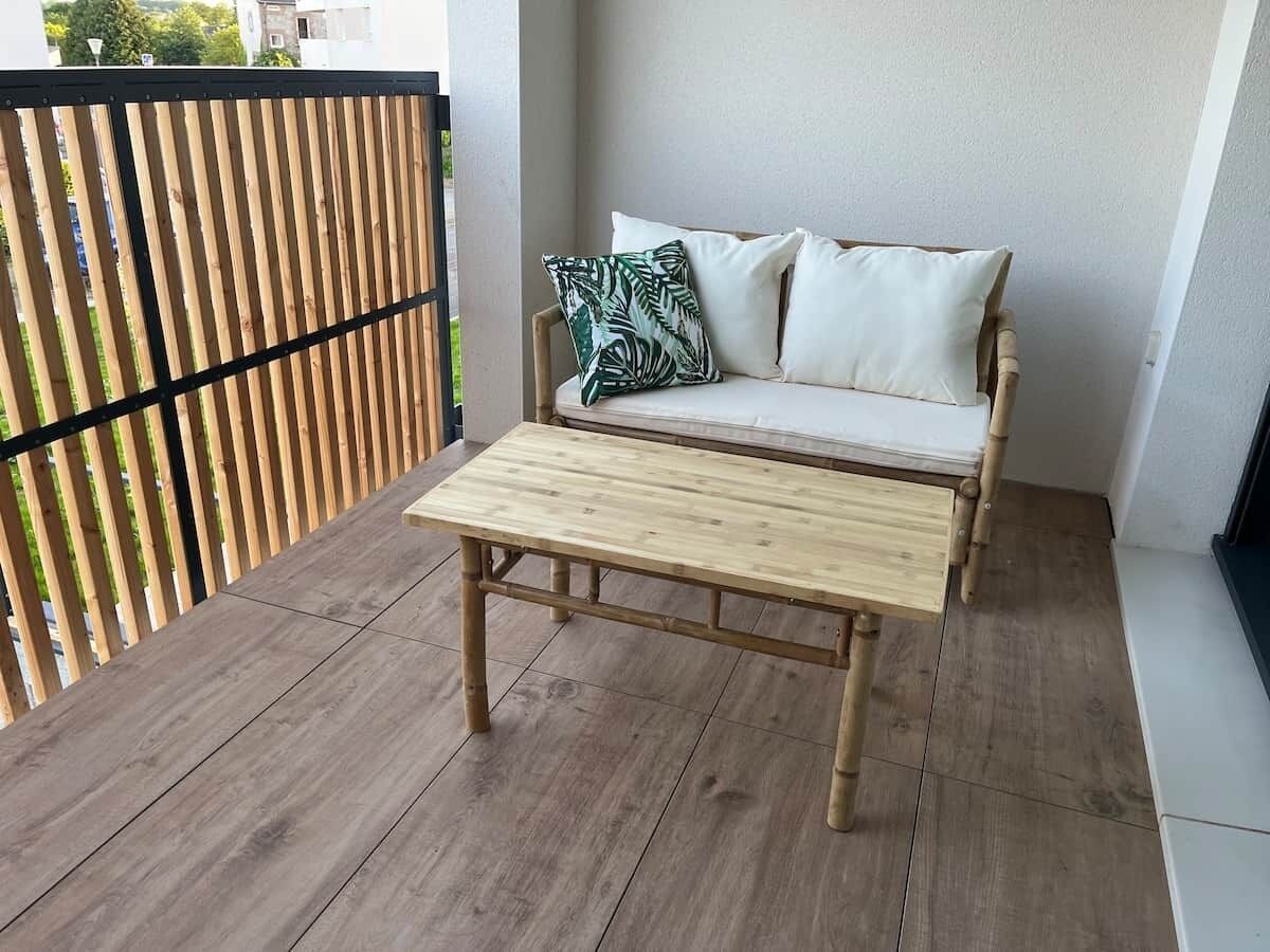 Un balcón con una mesa de madera y un sofá con cojines.