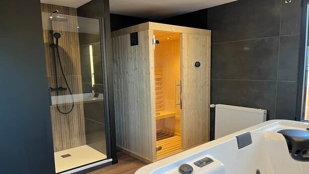 Moderni kylpyhuone, jossa on lasiseinäinen suihkukaappi, puinen sauna ja valkoinen kylpyamme.