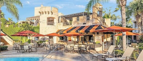 A pool area with lounge chairs and umbrellas, a bar, and a building with a curved facade.