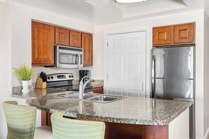 A kitchen with wooden cabinets, a stainless steel refrigerator, a microwave, and a granite countertop. - 3 Bedroom Villa at Grande Vista Resort w/Amenities (Orlando)