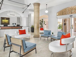 Un vestíbulo con mostrador de recepción, zona de estar con sillas y sofás, un pilar grande y un muro decorativo.
