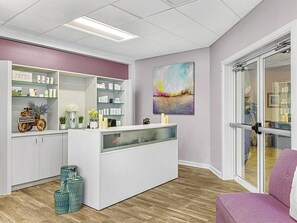 A reception area with a white reception desk, shelves with products, a glass door entrance, and a colorful abstract painting on the wall. - 3 Bedroom Villa at Grande Vista Resort w/Amenities (Orlando)