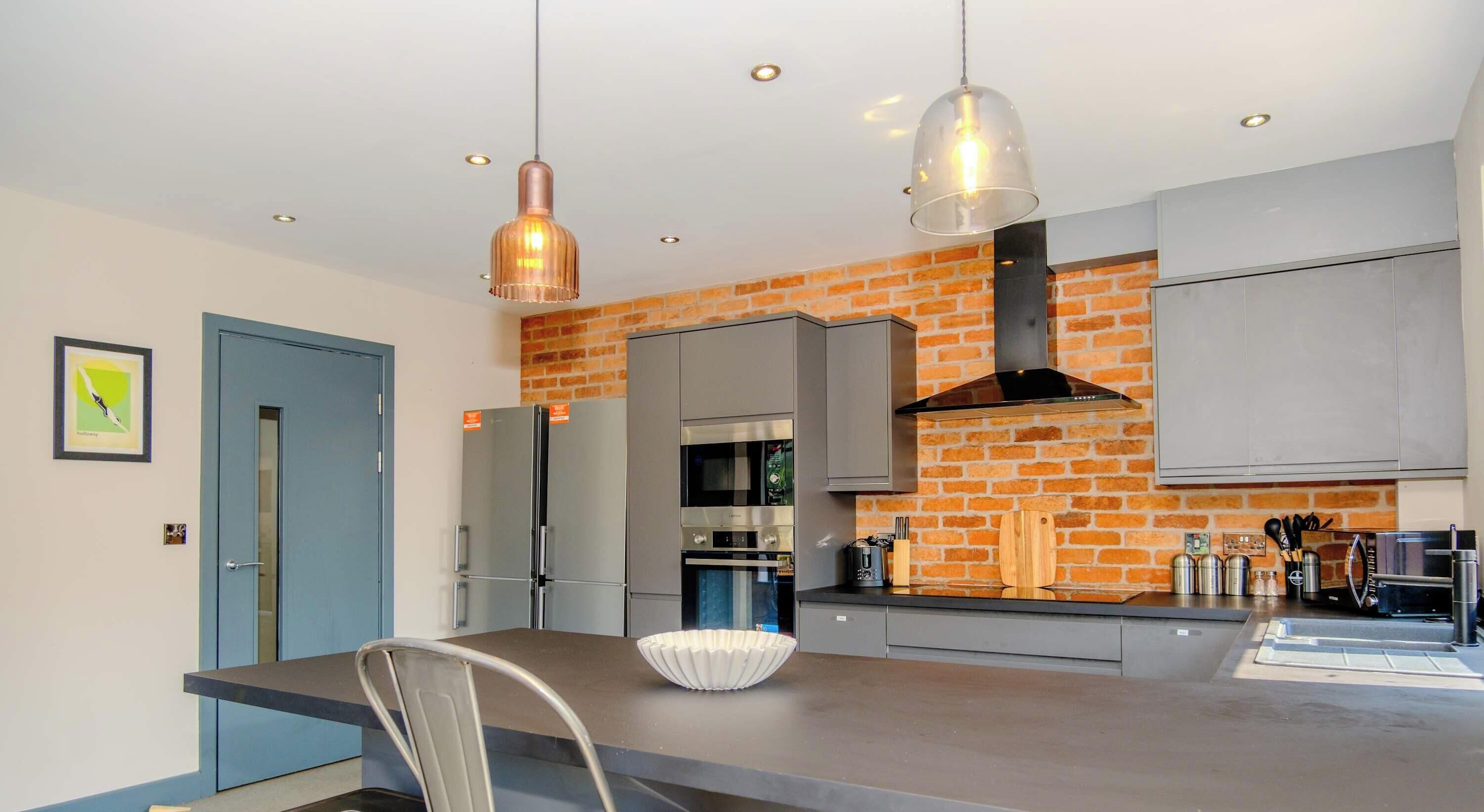 A modern kitchen with a brick wall, stainless steel appliances, and pendant lighting.