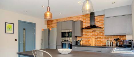 A modern kitchen with a brick wall, stainless steel appliances, and pendant lighting.