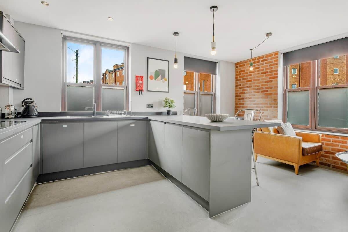 A modern kitchen with grey cabinets, a central island, and a seating area with a sofa and chairs.