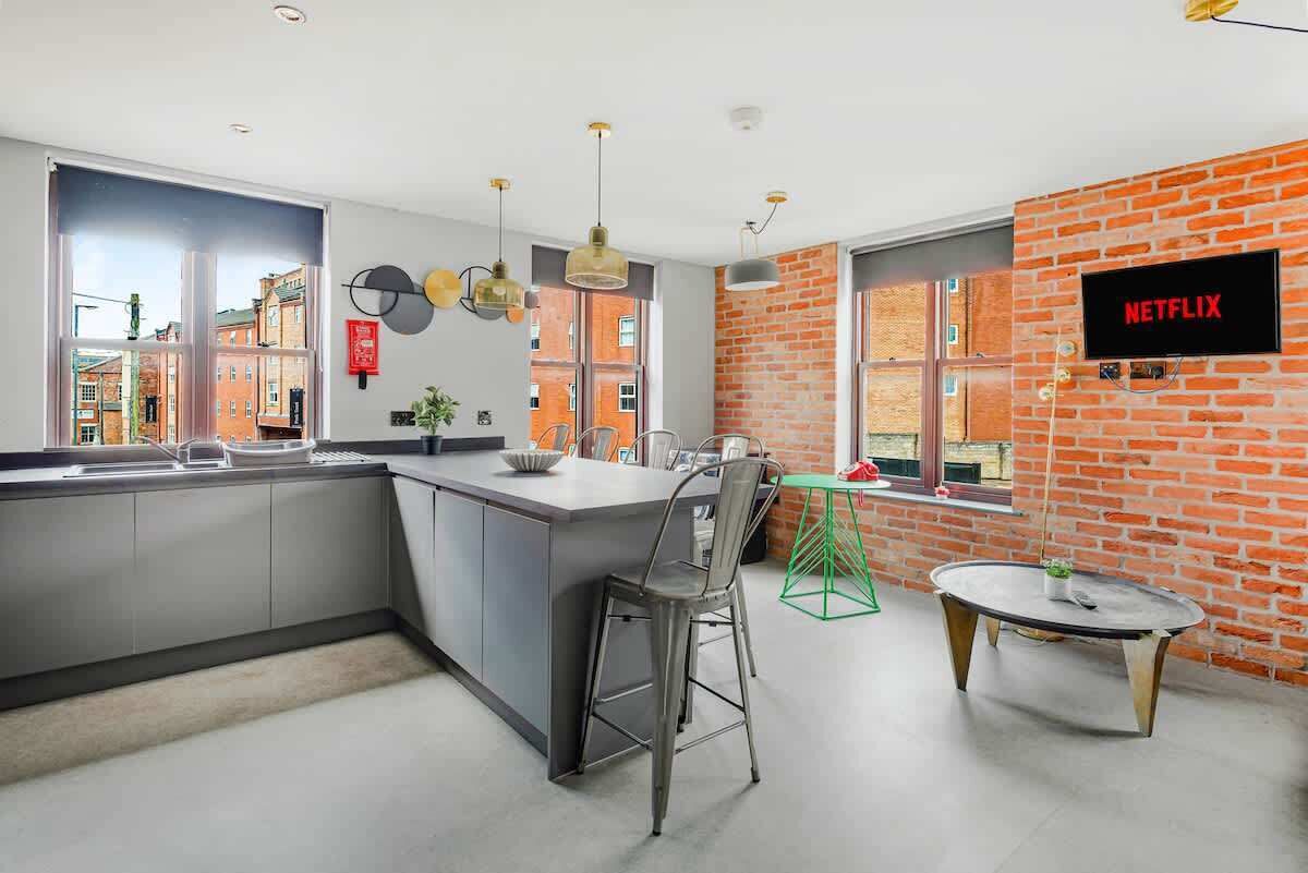 A modern kitchen with a large island, bar stools, a round table, and a brick accent wall.
