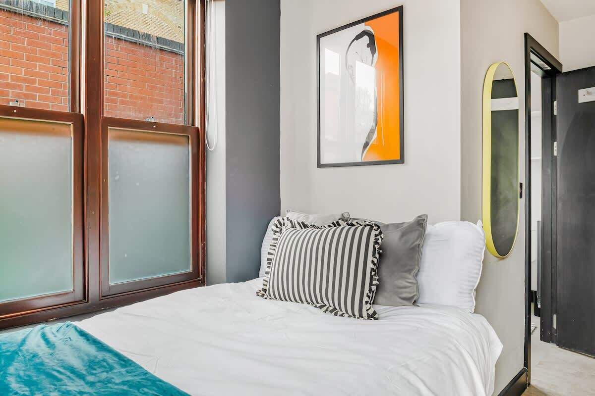 Un dormitorio con cama, ventana, puerta y una obra de arte colgada en la pared.